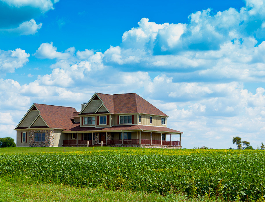 A rural house next to a field of green crops with cloudy sky