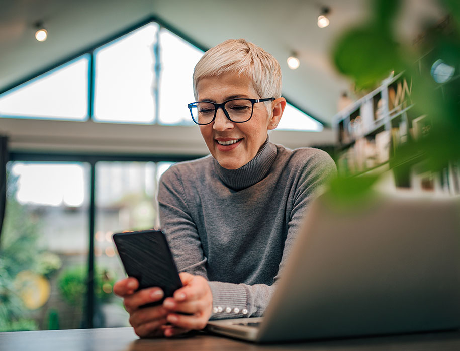 Woman using phone and laptop at desk at home