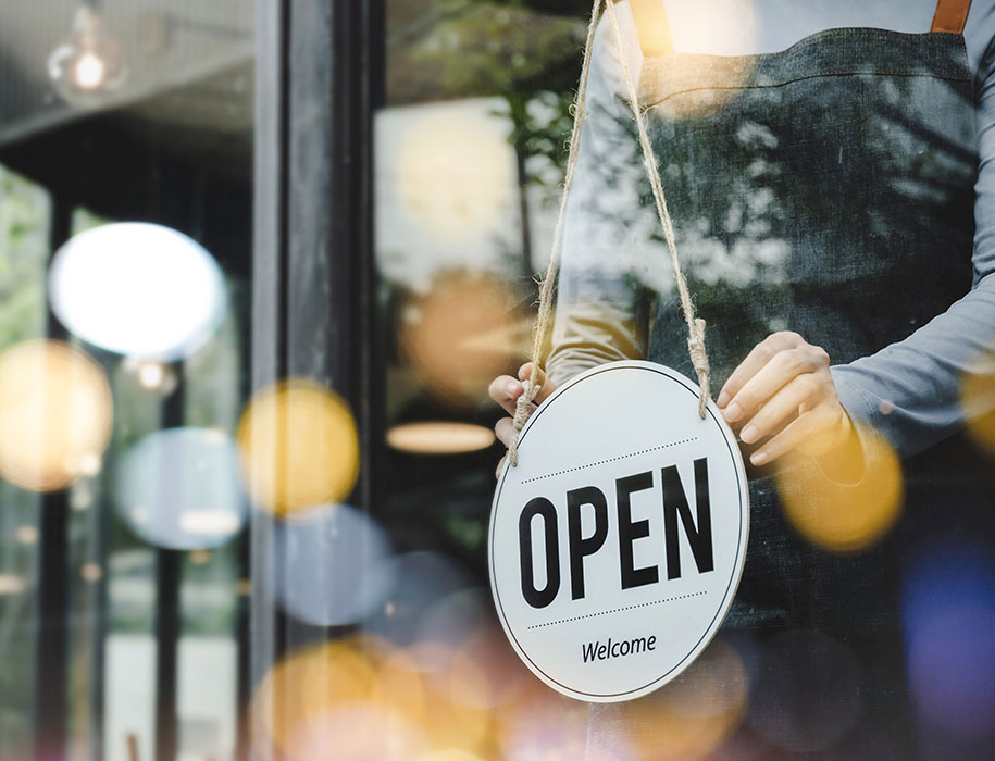 Person hanging an open sign in business store front